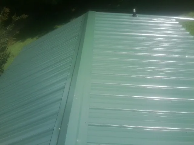 New green metal panels meeting at the ridge of a roof — Flat Roof Repair work by our crew in Cameron